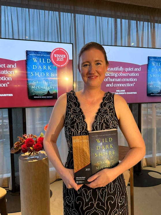 Author Charlotte McConaghy holding the Dymocks Book of the Year trophy and her book, Wild Dark Shore.