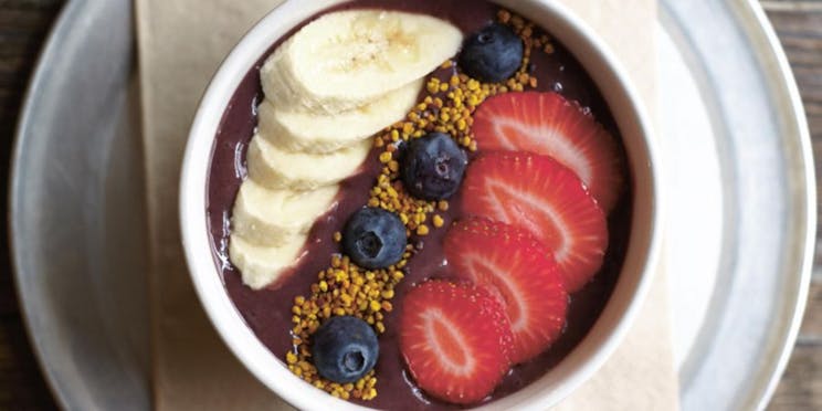 Overhead view of an acai bowl, topped with banana, berries and bee pollen. 