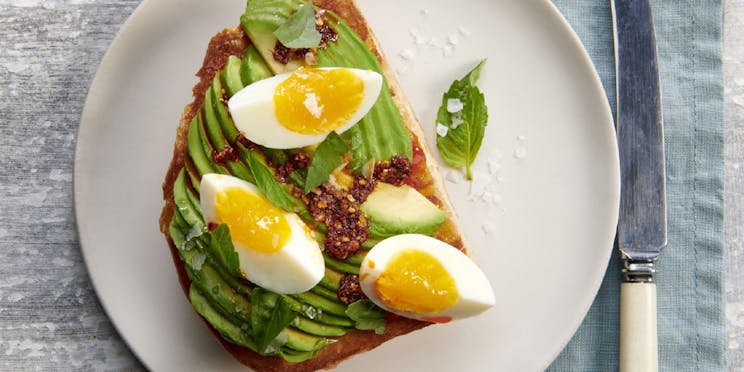 Overhead shot of avocado toast on a white plate with boiled eggs. 