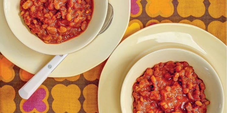 Overhead view of two bowls of baked beans against a floral patterned tablecloth. 