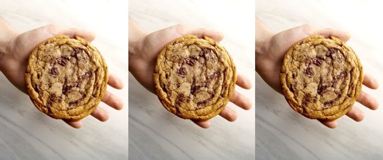 A hand holding a chocolate chip cookie, the photo is tiled 3 times across the banner.