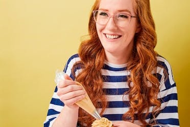 Photo of baker Jane Dunn holding a piping bag, with a yellow background. 