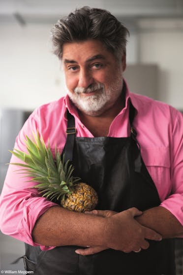 Chef Matt Preston wearing a pink shirt and apron, holding a pineapple.