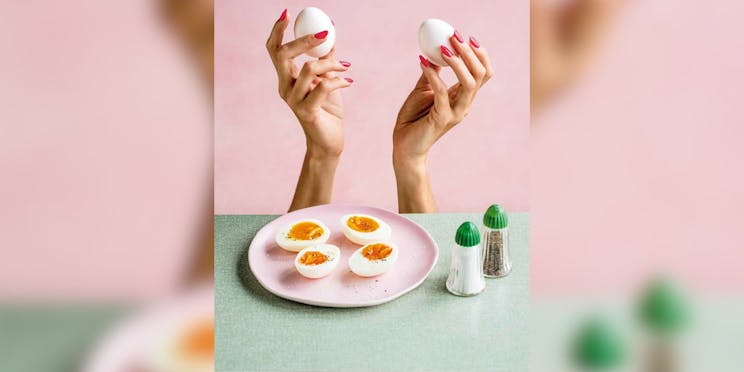 Eggs on a pink plate with two hands holding eggs in the background. 