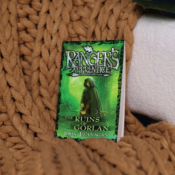 Ranger's Apprentice book one, sitting on a chair draped with a brown knitted blanket. 
