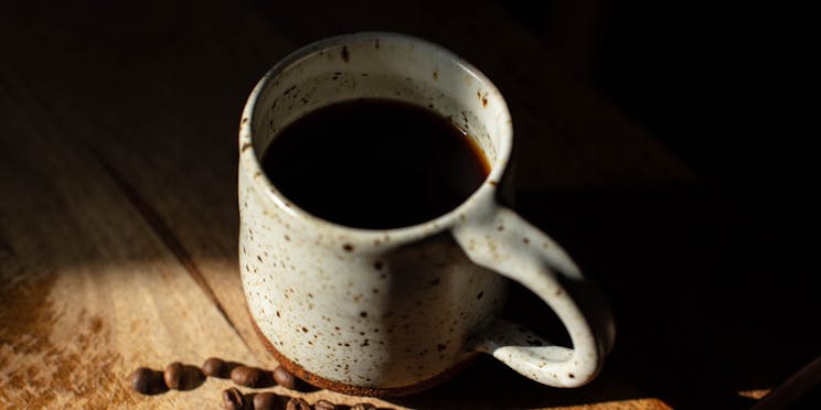 Angled view of a mug of black coffee on a wooden table. 